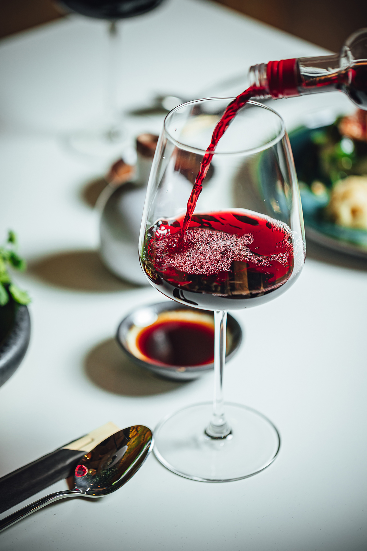 Glas Rotwein wird eingeschenkt; im Hintergrund sind Speisen zu erkennen.