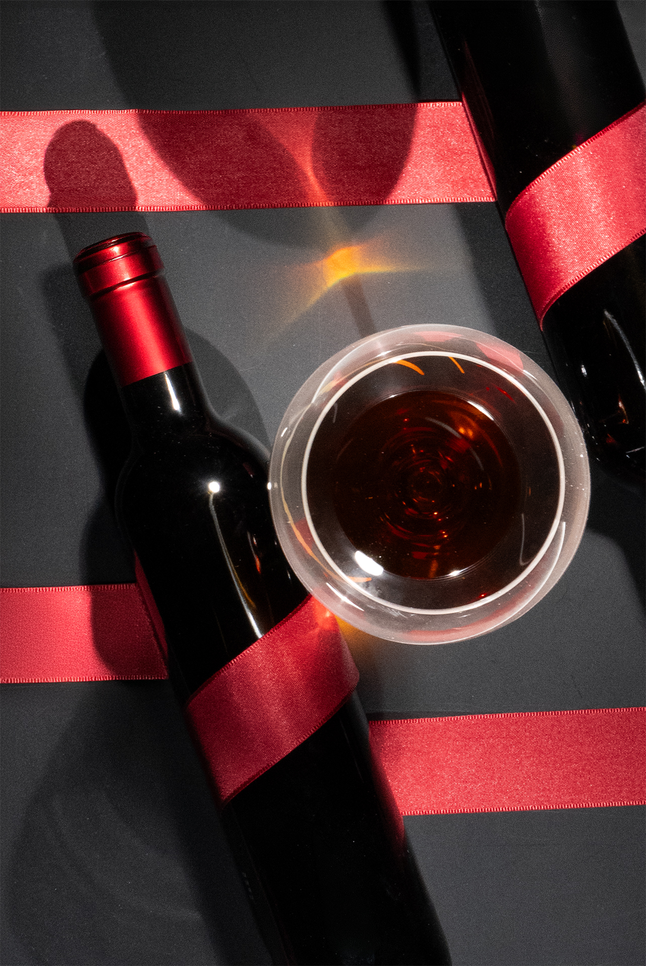 Rotweinflasche und Rotwein im Glas mit Geschenkband.